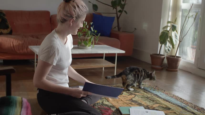 A woman sitting on the floor pets her cat as it walks by