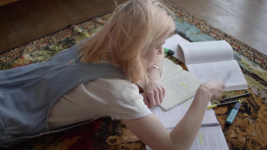A teenager lies on the floor and does homework
