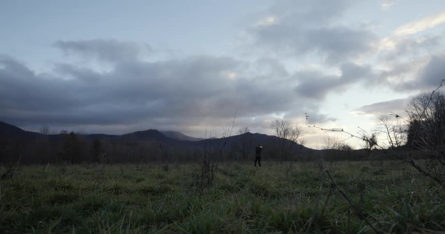 Young woman taking pictures of the mountains in the grass fields at evening