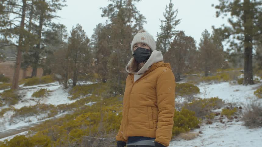 A woman is standing outdoors in a forest during winter