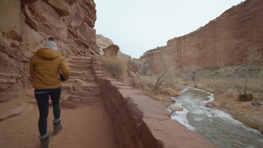 Woman wearing winter clothing walking through a canyon with a river on her side
