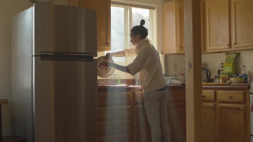 Woman with white sweater and jeans does the dishes in the kitchen