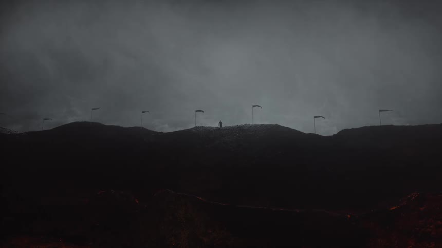 A person climbs up at the top of a hill where flag post are waving in the wind