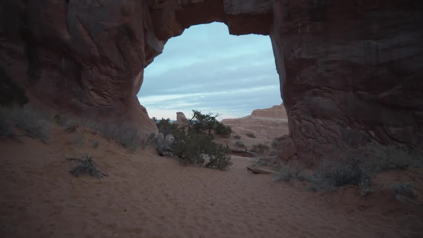 A natural arch rock formation in a desert above plants at daytime