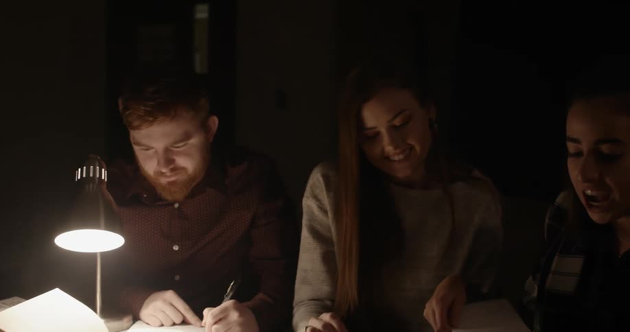 Group of friends studying and taking notes on a dimly lit room