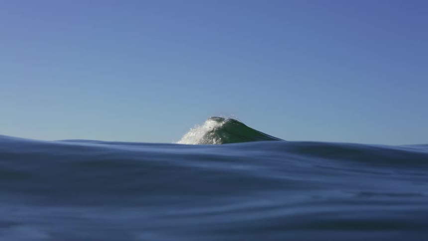 A wave breaks in the ocean on a sunny day