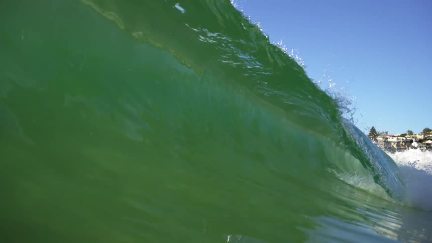Small wave of green ocean water crashing in the coast near a town