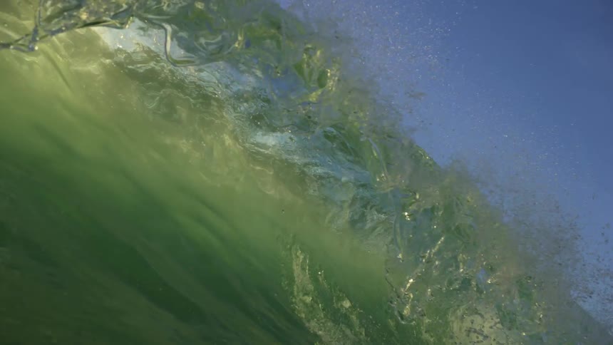 A bluegreen wave crashes in the ocean on a sunny day