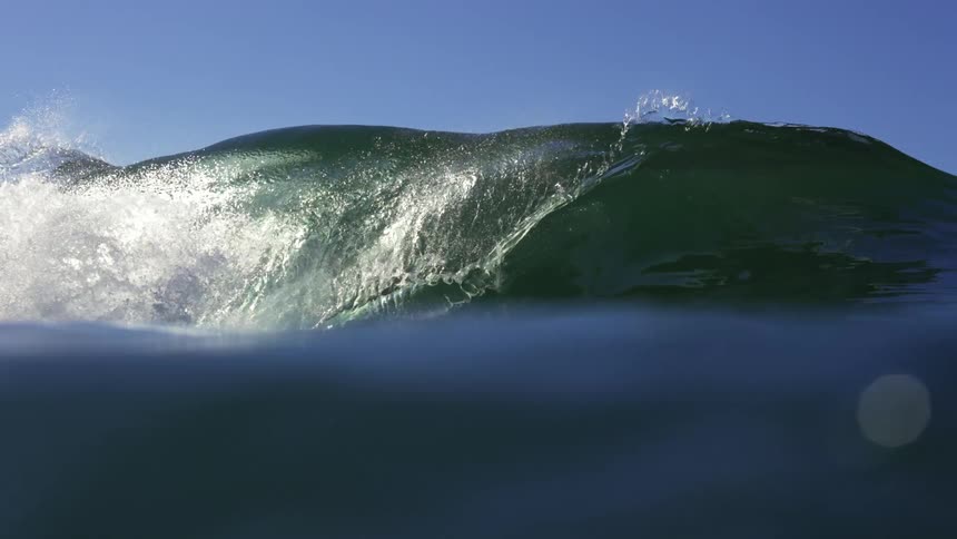 Wind wave breaking over the blue surface of the green ocean waters