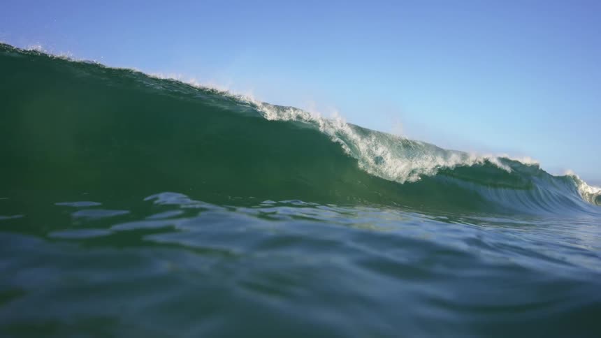A wave of water in the ocean with the sky and clouds in the background
