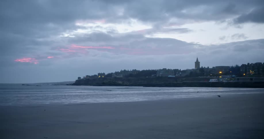 A beach with a small town over in the distance in the evening