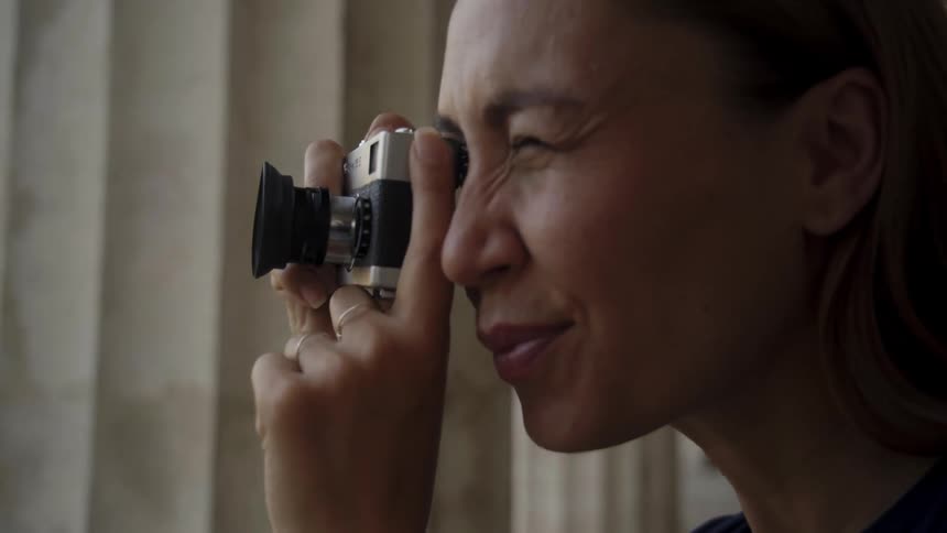 Young woman uses a vintage camera to take photographs of a building