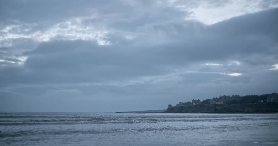 Waves roll in on shoreline a cloudy day with buildings along the coast