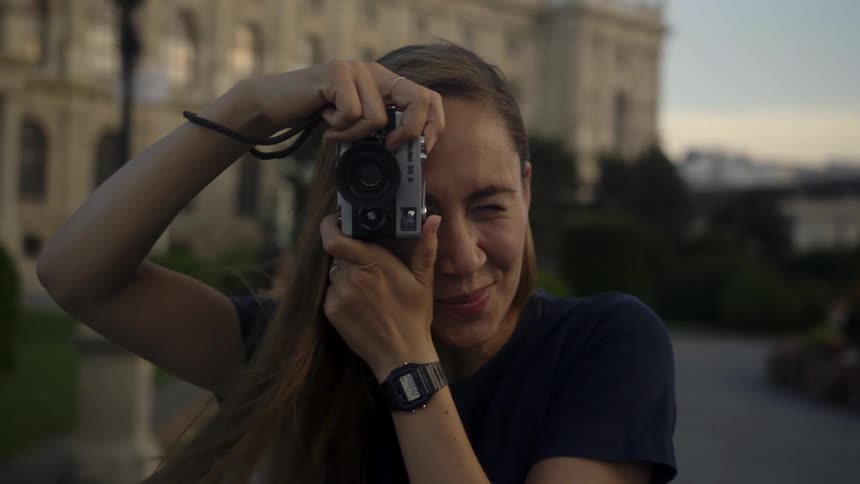 Woman takes pictures vintage film camera while looking at the camera at sunset