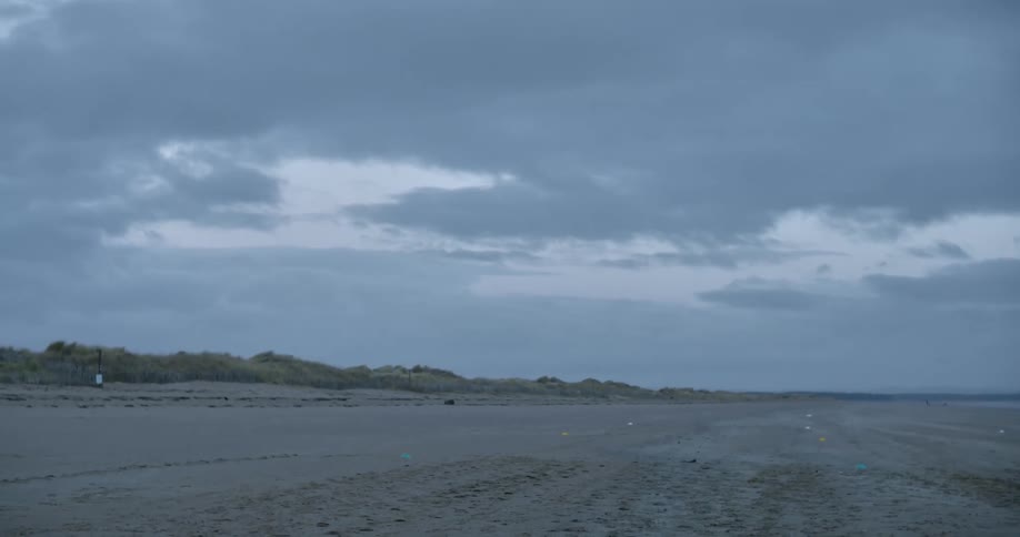 A beach in the evening with one person walking in the distance