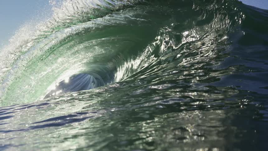 A wave of water in the ocean with the sky and clouds in the background