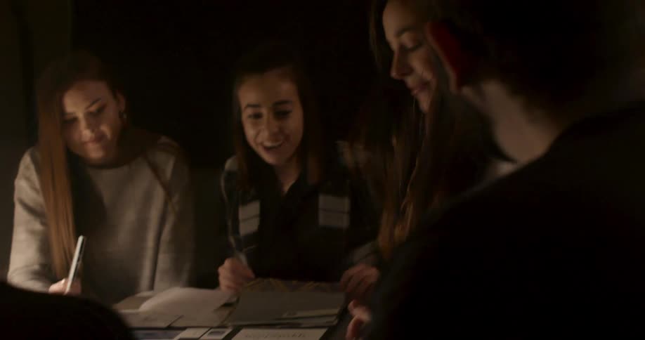 A teenage girl walks to a table and sits down with a group of other teens