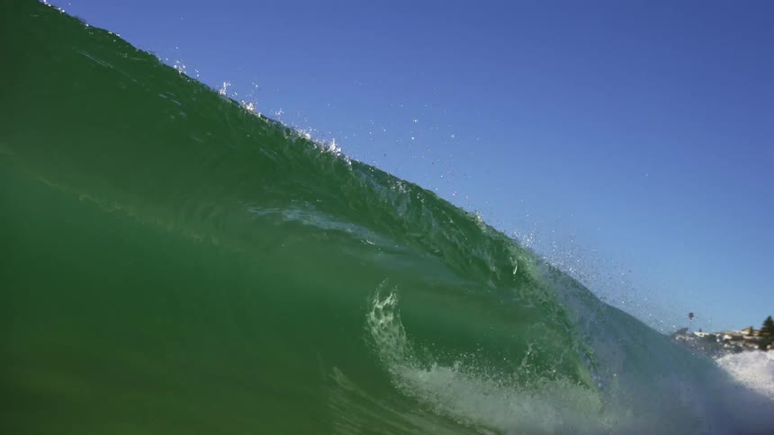 Green ocean wave crashing in the coast near a small town at day time
