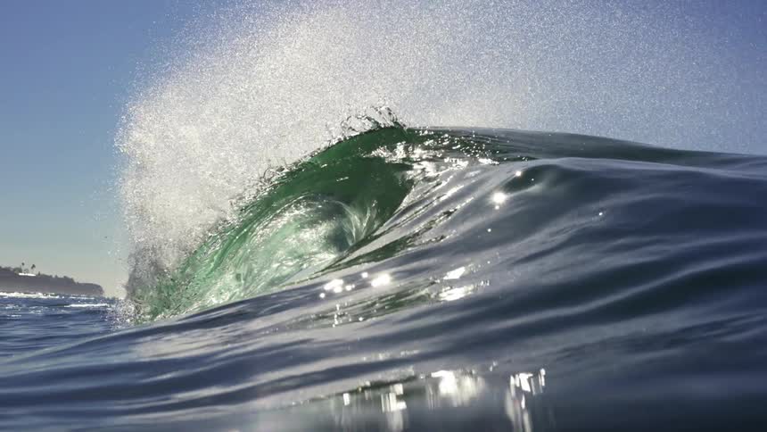 Ocean wave rolls in and overhead splashing on a clear day