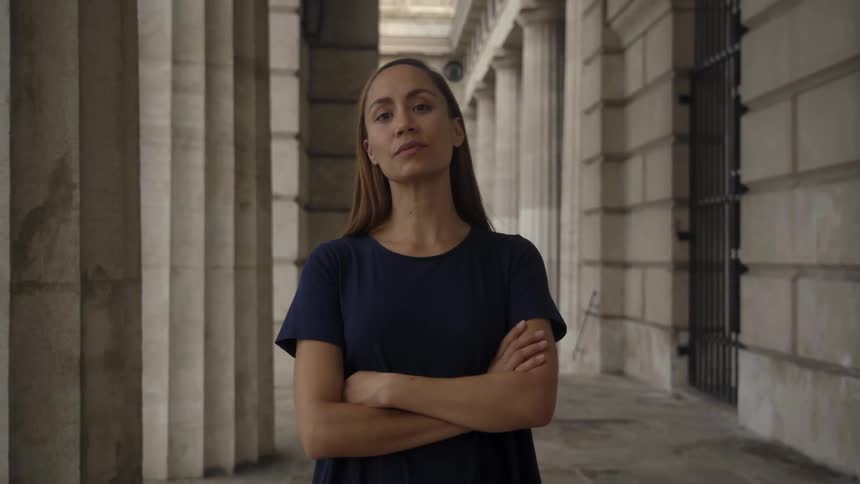 A woman stands inside building crossing her arms while looking at the camera