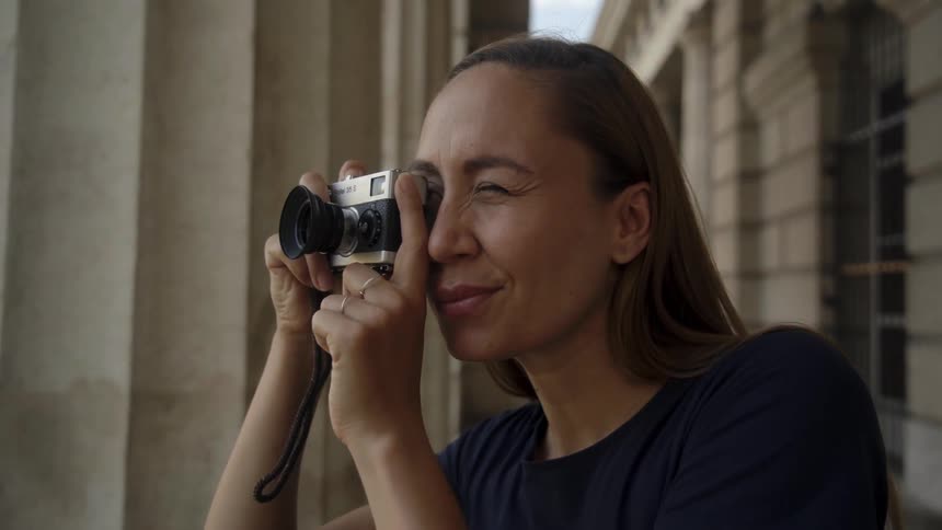 A woman uses a small camera to take a picture out under a column structure at daytime