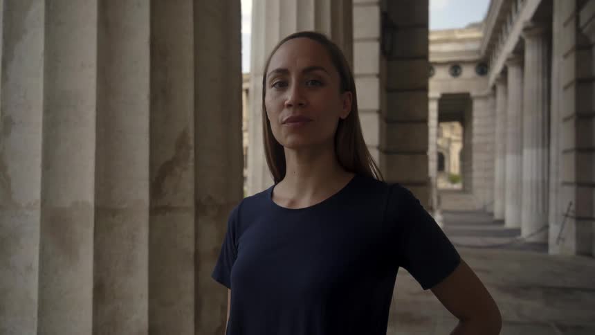 Woman standing next to the columns of a building turns around to look at the camera