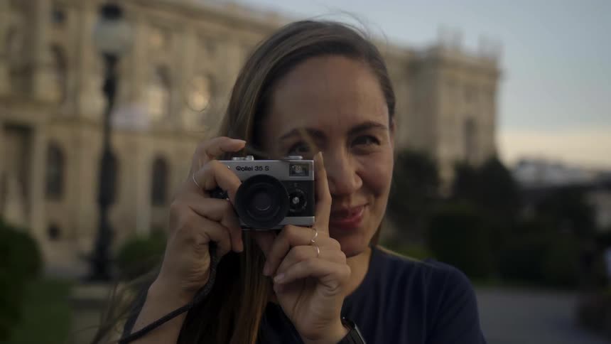 Young woman takes pictures of the cameraman with a vintage camera at sunset