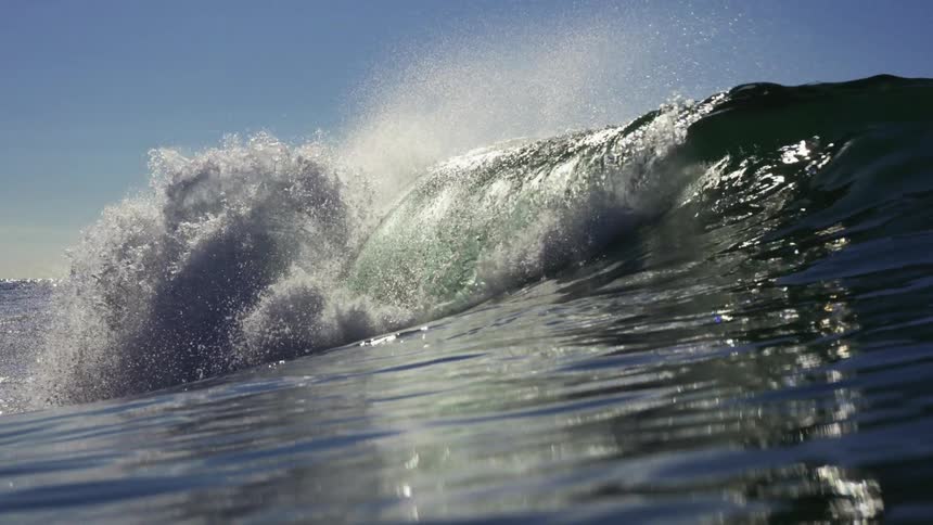 A wave in the ocean with water splashing with the sky and clouds in the background