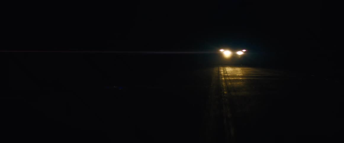 The flare of car lights as it drives at night