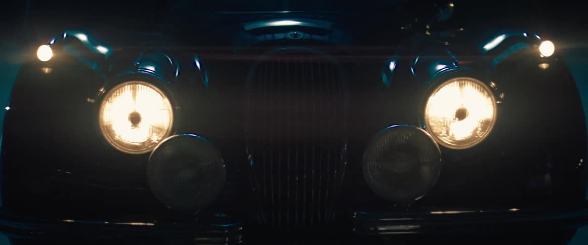 Vintage vehicle parked outdoors at night turning on the headlights