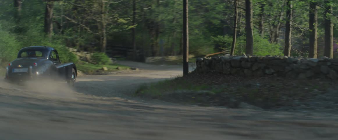 A man drives a vintage car down a dirt road