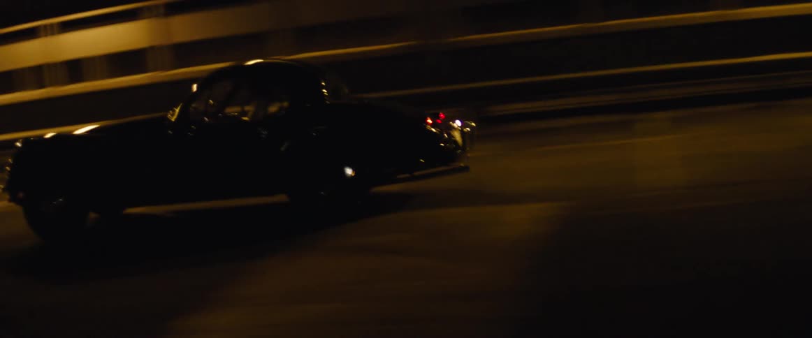 A black antique car being driven in a dark parking garage