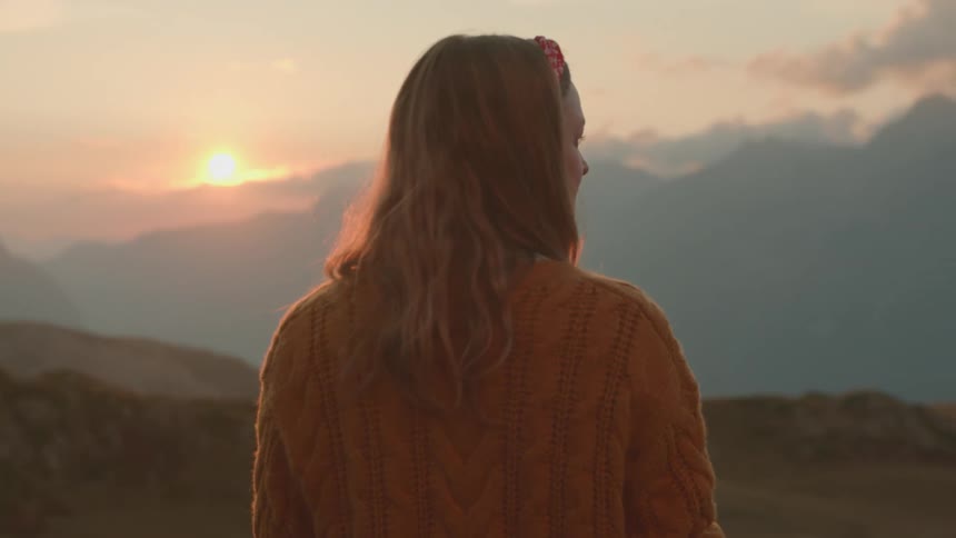 Woman wearing sweater stands looking at scenic view