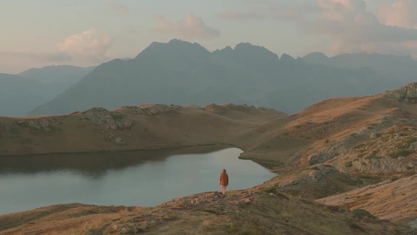 A woman stands on a hill on the shore and looks at the lake