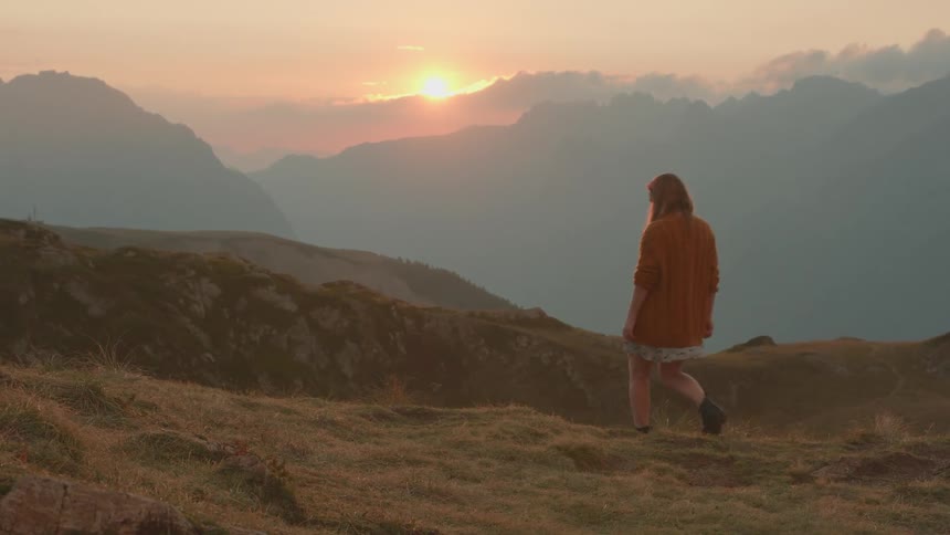 Young woman sitting over the grass in the slope of a mountain contemplating the sunset over the clouds