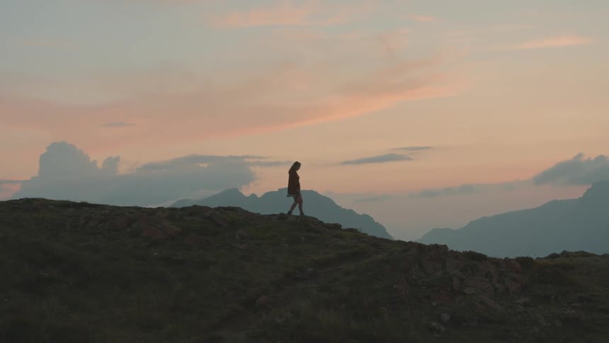 A silhouetted hiker walking on a hill at sunrise