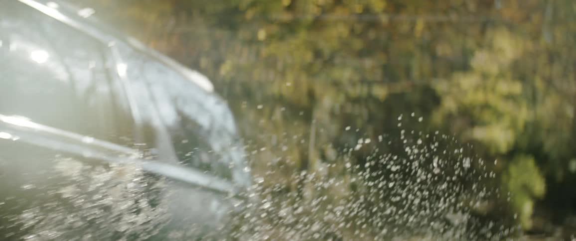 Light glare reflects off windows of suv fording river in forest