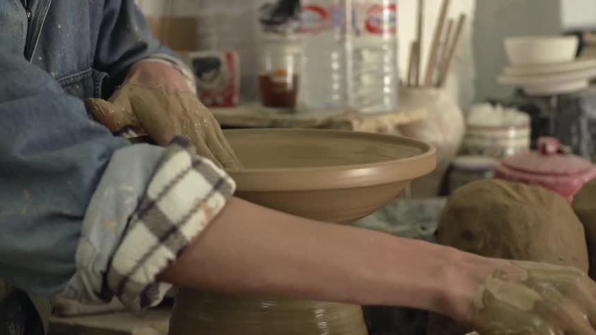 A person is making pottery indoors during the day