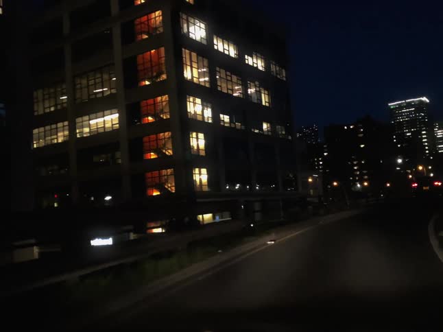 A car drives on a highway on a ramp in a city setting at night