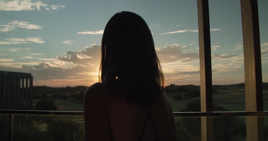 A woman is standing outdoors and watching the sun set