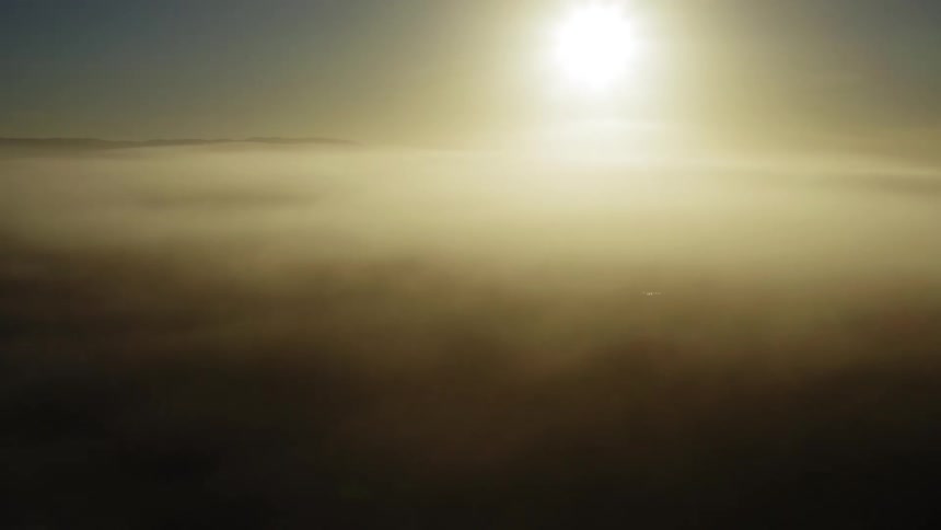 The sun in the sky with clouds and a mountain range in the background