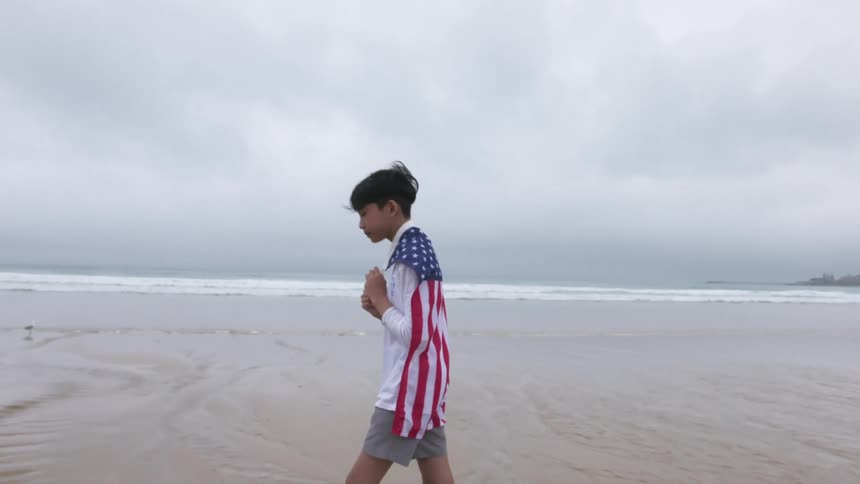 A child is walking on the beach with an american flag