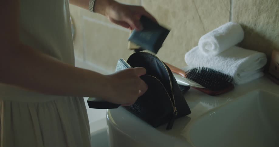 Woman takes items out of makeup bag standing near sink