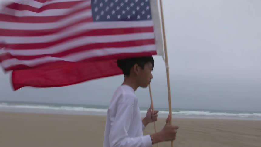 Young asian teenager carrying an american and china flags on a beach on a windy day