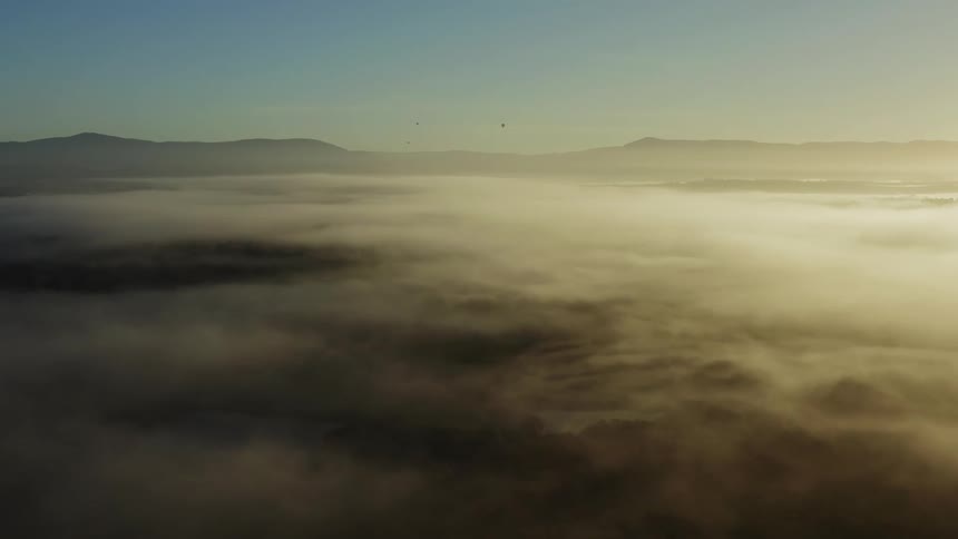 Clouds moving by high in the sky with mountains on the horizon and three balloons in the sky