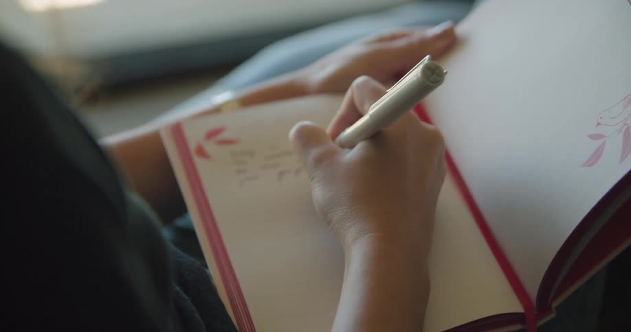 A woman sits inside and writes in a book