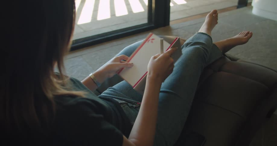 A woman sitting on a couch with a book and pen