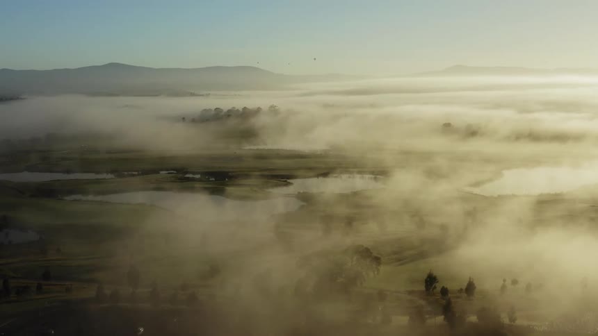 An aerial view of a landscape covered in fog is displayed