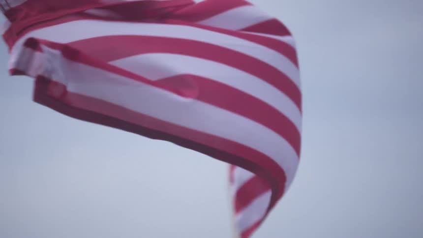 An american flag waving in the wind with the sky and clouds in the background
