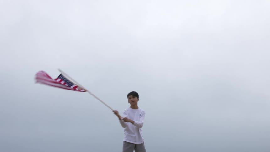 A young boy standing outside waving the american flag